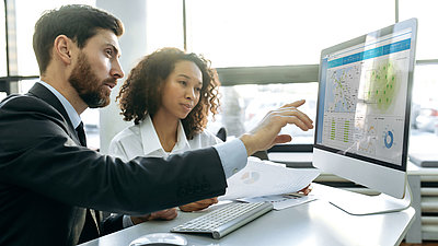 Two employees look at a monitor showing the LANCOM Management Cloud