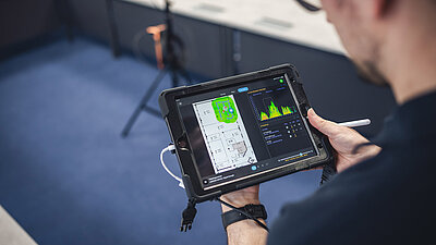 Man at the tablet with pen in hand, showing a frequency spectrum in green including a floor plan