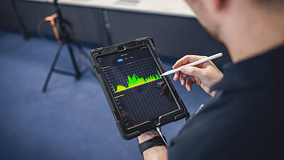 Man at the tablet with pen in hand, showing a frequency spectrum in green