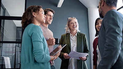 Photo of a cheerful working group of five casually dressed people in the office, having a good-humored standing conversation