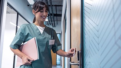 Photo: Healthcare employee opening a secured door with an access card, representing digital access rights and modern access control in sensitive critical infrastructure environments.