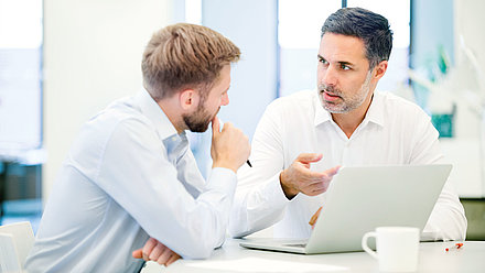 Two office workers talking seriously in front of laptop in office