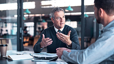 Two people sit at an office table and discuss