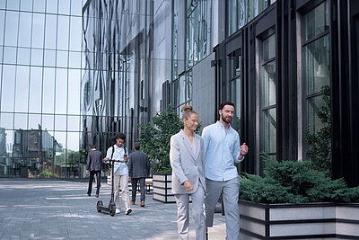 Glass facade of an office complex with employees walking past it