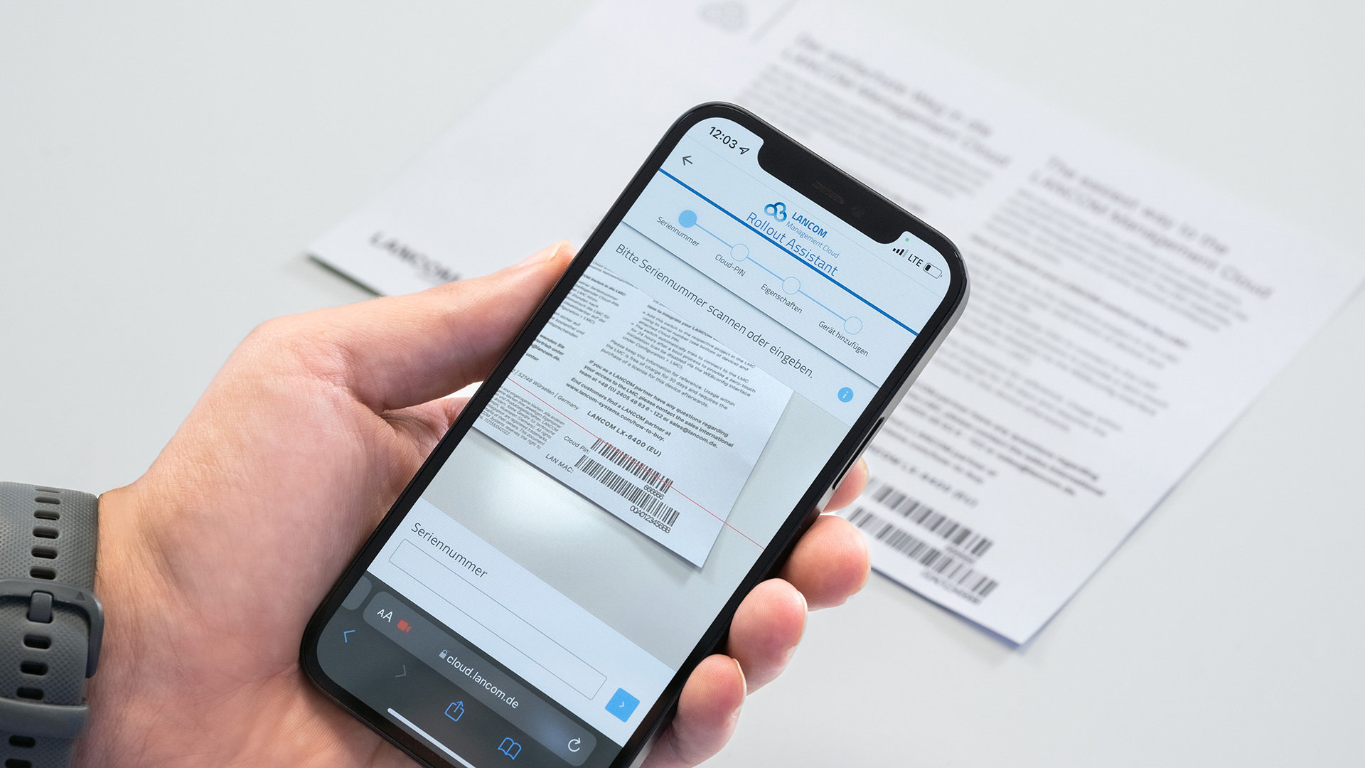 Hand hält Smartphone und scannt damit Barcode vom LANCOM cloud-ready Beileger ein