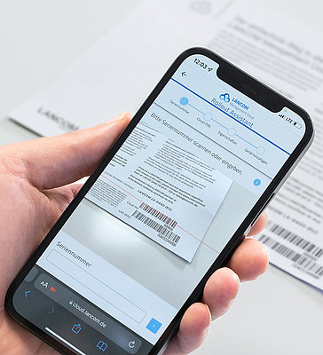 Hand holds smartphone and uses it to scan barcode from LANCOM cloud-ready enclosure