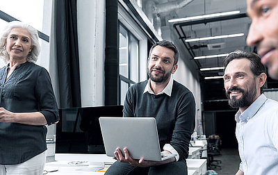 Group of four motivated, attentive employees of different ages and genders sitting in meeting and smiling approvingly