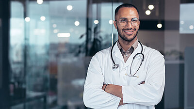 Man in a doctor's coat with his arms crossed smiles at the camera
