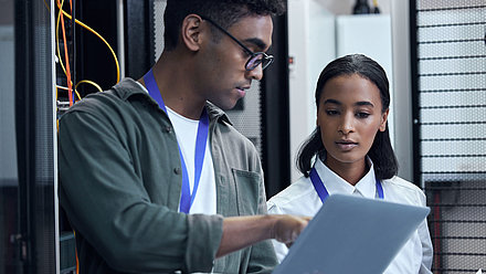 Male and female IT administrators confer on laptop in server room for better network management