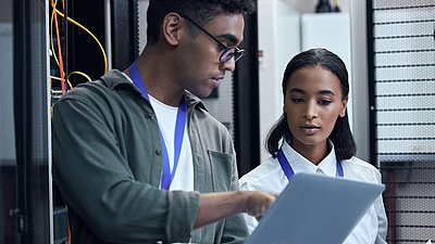 With the LANCOM Management Cloud to optimized network management Male and female IT administrators confer on laptop in server room for better network management
