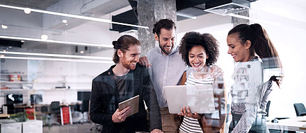 Group of young office workers looking at a laptop together in modern office