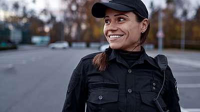 Photo: Female security officer in a black uniform with a radio carefully monitoring an outdoor area, representing secure surveillance and protection concepts in critical infrastructures.