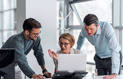 Group of three administrative employees sits in office at laptop and consults with each other