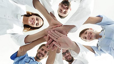 Healthcare team stacking hands and smiling, symbolizing collaboration and teamwork in a medical setting.
