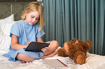 Little girl watches movie on tablet with her teddy in hospital bed