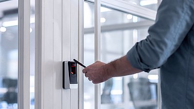 Photo: Person using a smartphone at an electronic access reader for secure access control in a modern building, illustrating digital security and access concepts for critical infrastructures.