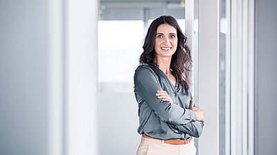 Woman leaning against a glass door with her arms crossed, smiling at the camera