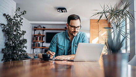 Man works on a notebook in his home office and writes down notes on a piece of paper