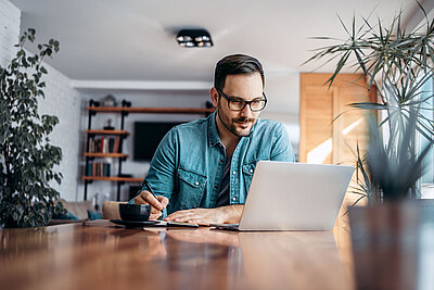 Man works on a notebook in his home office and writes down notes on a piece of paper