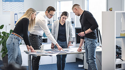 Colleagues standing in front of a table on which pictures are spread out and discussing their picture selection