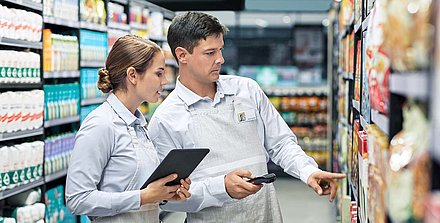 A supermarket employee with a tablet checks the goods on the shelf with her colleague with a handheld scanner