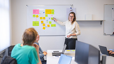 An intern shows her colleagues something on the whiteboard