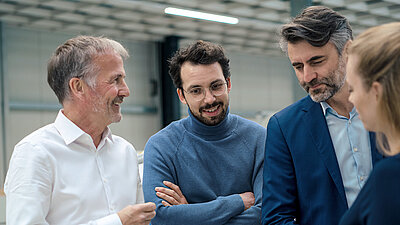 Four business professionals in discussion, smiling and focused in a modern technical setting.