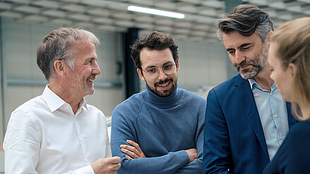 Four business professionals in discussion, smiling and focused in a modern technical setting.
