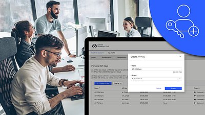 Image with focus on screenshot of the new API application on a monitor, icon, and people in the office in the background