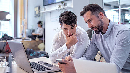 Man working in home office showing teenage son something on smartphone