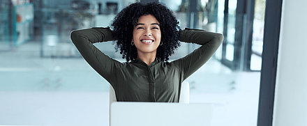 Office worker sits relaxed at her desk with arms folded behind her head because her Wi-Fi optimizes itself with LANCOM Active Radio Control 2.0