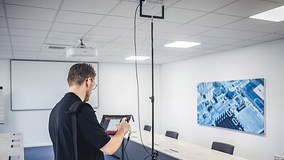 Technician stands with his back to the viewer in front of a tripod with an access point and looks at a tablet