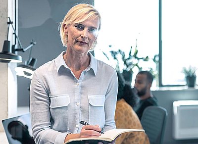 Blonde, middle-aged franchisor stands in office at headquarters and checks off checklist