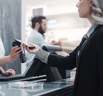 Blonde customer in black blazer pays contactless with her smartphone at the checkout of a modern store