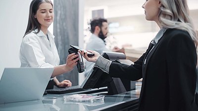 Blonde customer in black blazer pays contactless with her smartphone at the checkout of a modern store