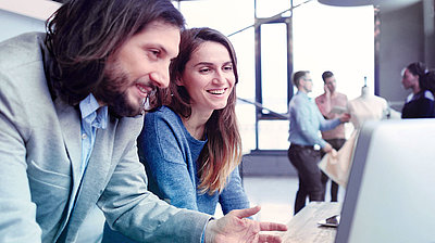 Woman and man laughing in front of PC screen in modern office