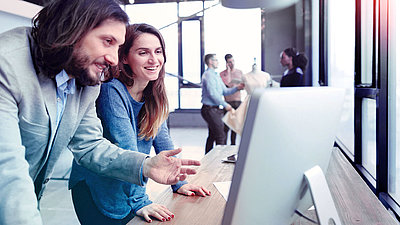 Woman and man laughing in front of PC screen in modern office