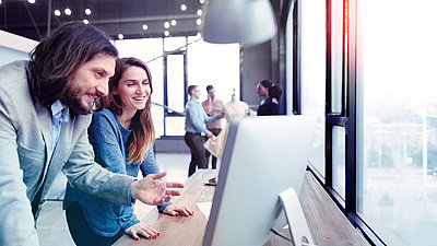 Man and woman laughing in front of PC screen in modern office