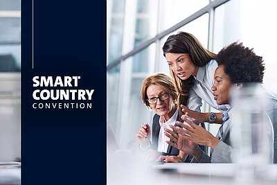 Three businesswomen discuss at a laptop, with the Smart Country Convention logo shown on the left.