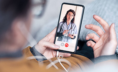 Man holding phone with headphones; he looks at the screen from above and attends a video call with a female doctor