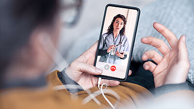 Man holding phone with headphones; he looks at the screen from above and attends a video call with a female doctor