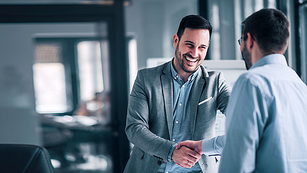 Two men in suits shake hands in a spirit of partnership