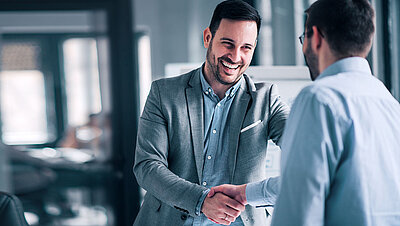 Two men in suits shake hands in a spirit of partnership