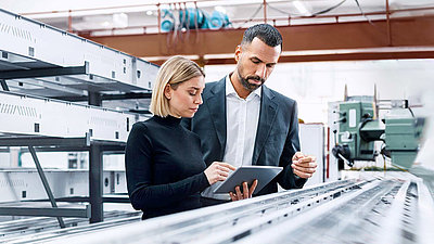 Two employees stand in a factory and use 5G mobile communications on a tablet