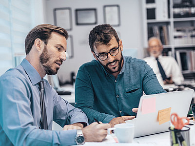 Two administrative employees confer in the office on a laptop about a digital file