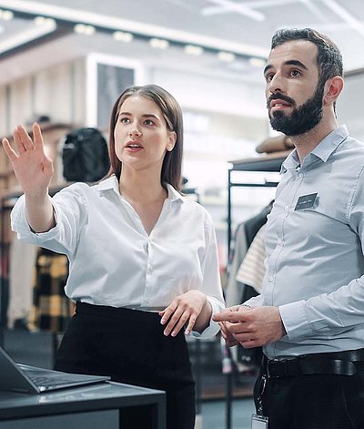 Brunette store manager in white blouse shows attentive employee where the next digital advertising banner will be placed in fashion store