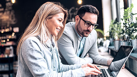 A man and a woman are looking at a laptop in a good mood. She is typing something.