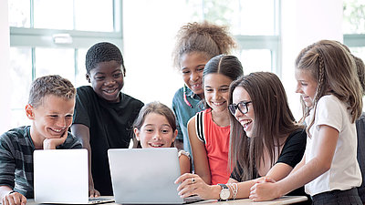 Elementary school teacher enthusiastically shows her students something on laptop