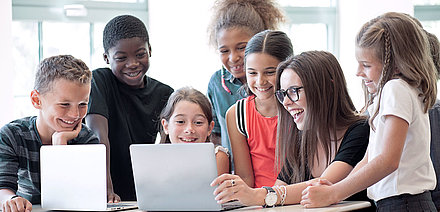 Elementary school teacher enthusiastically shows her students something on laptop
