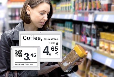Brunette woman looking at instant coffee from shop-in-shop coffee shelf with electronic price tags in supermarket with enlarged view of two displays in lower left corner of image